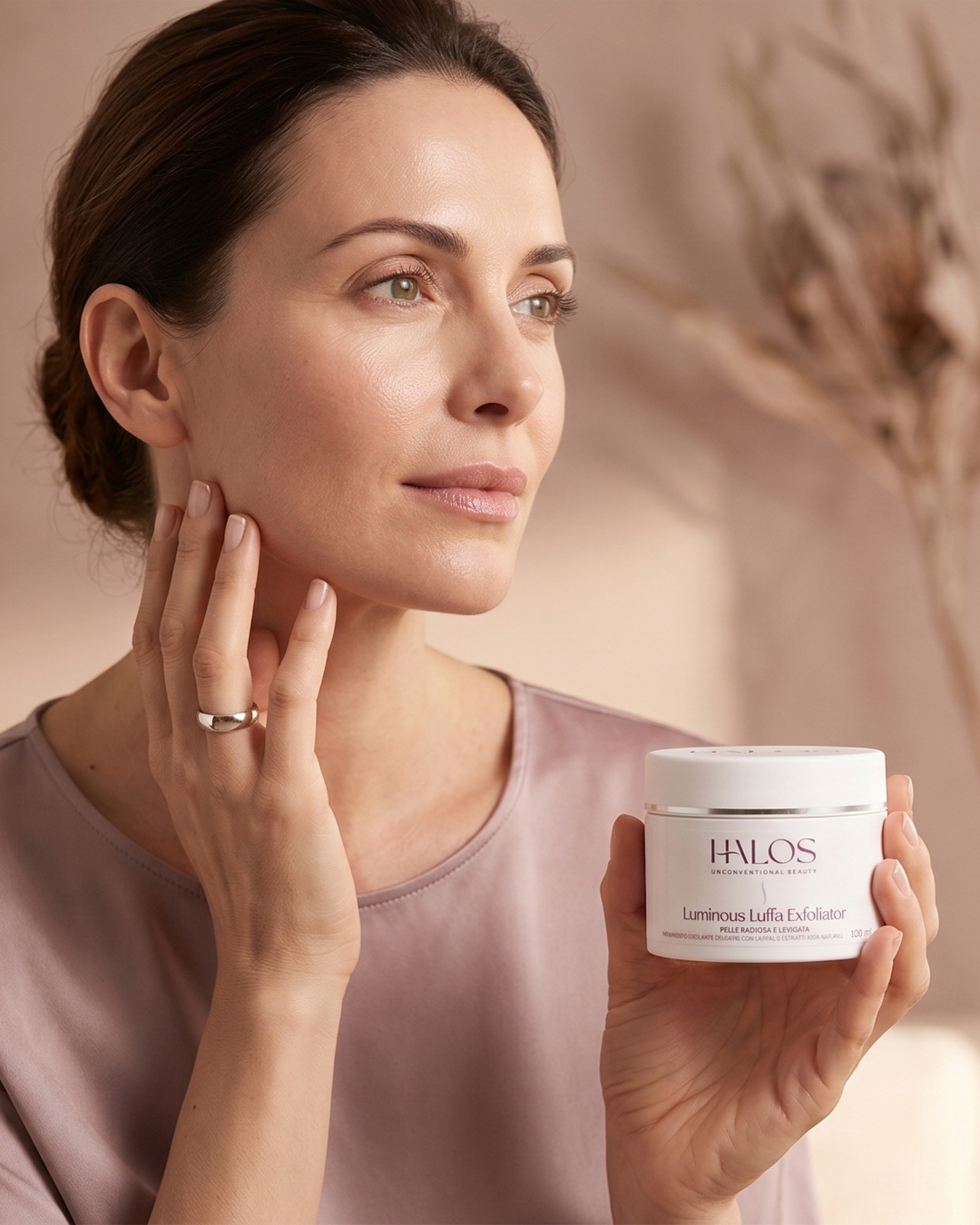 Donna che tocca la mandibola tenendo il vasetto di Luminous Luffa Exfoliator