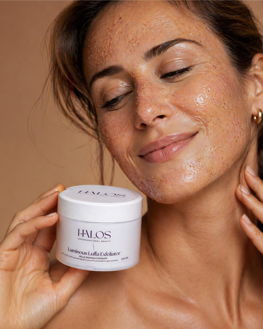 Donna con Luminous Luffa Exfoliator applicato sul viso e vasetto in mano