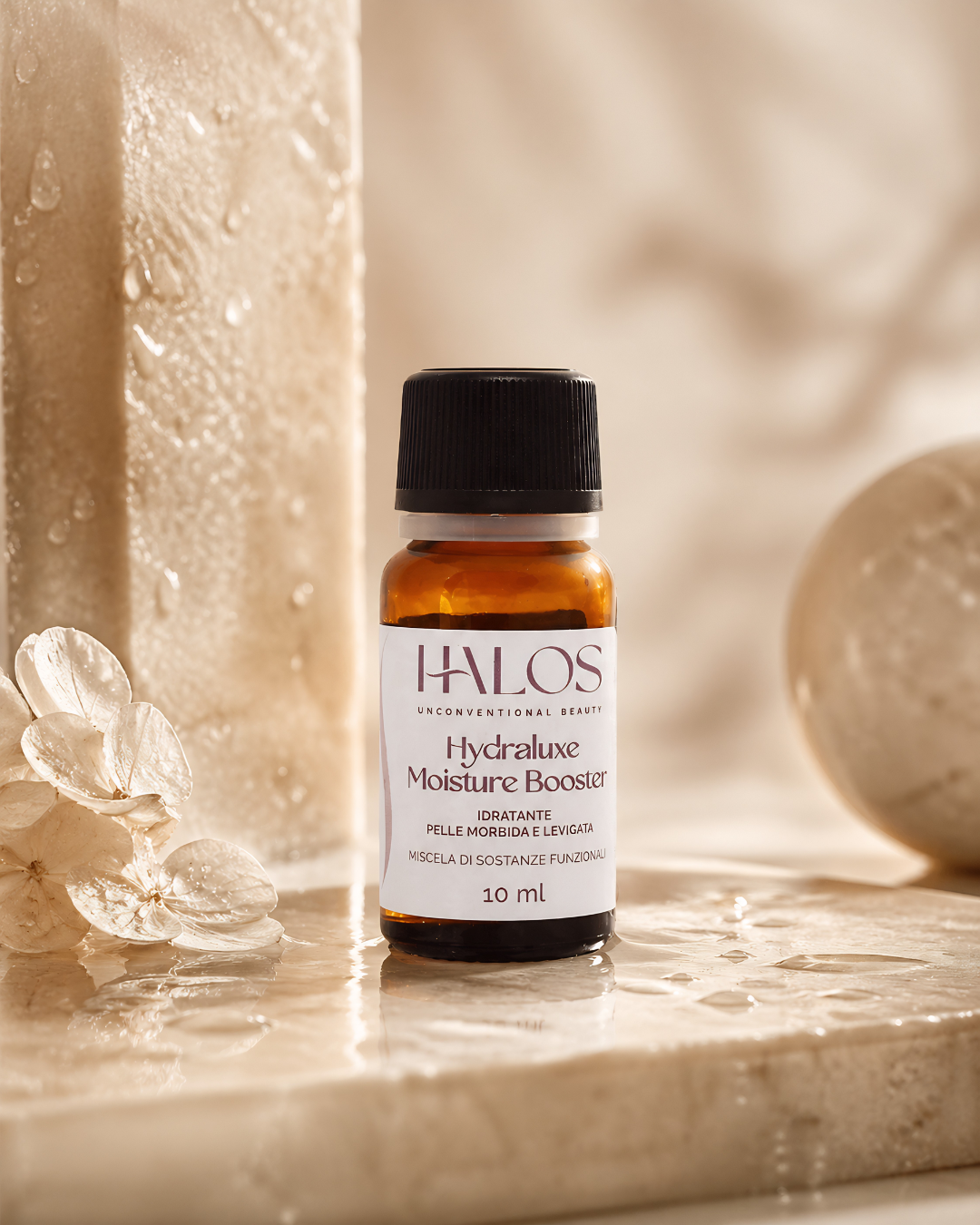 Flacone di Hydraluxe Moisture Booster tra gocce d’acqua e decorazioni trasparenti