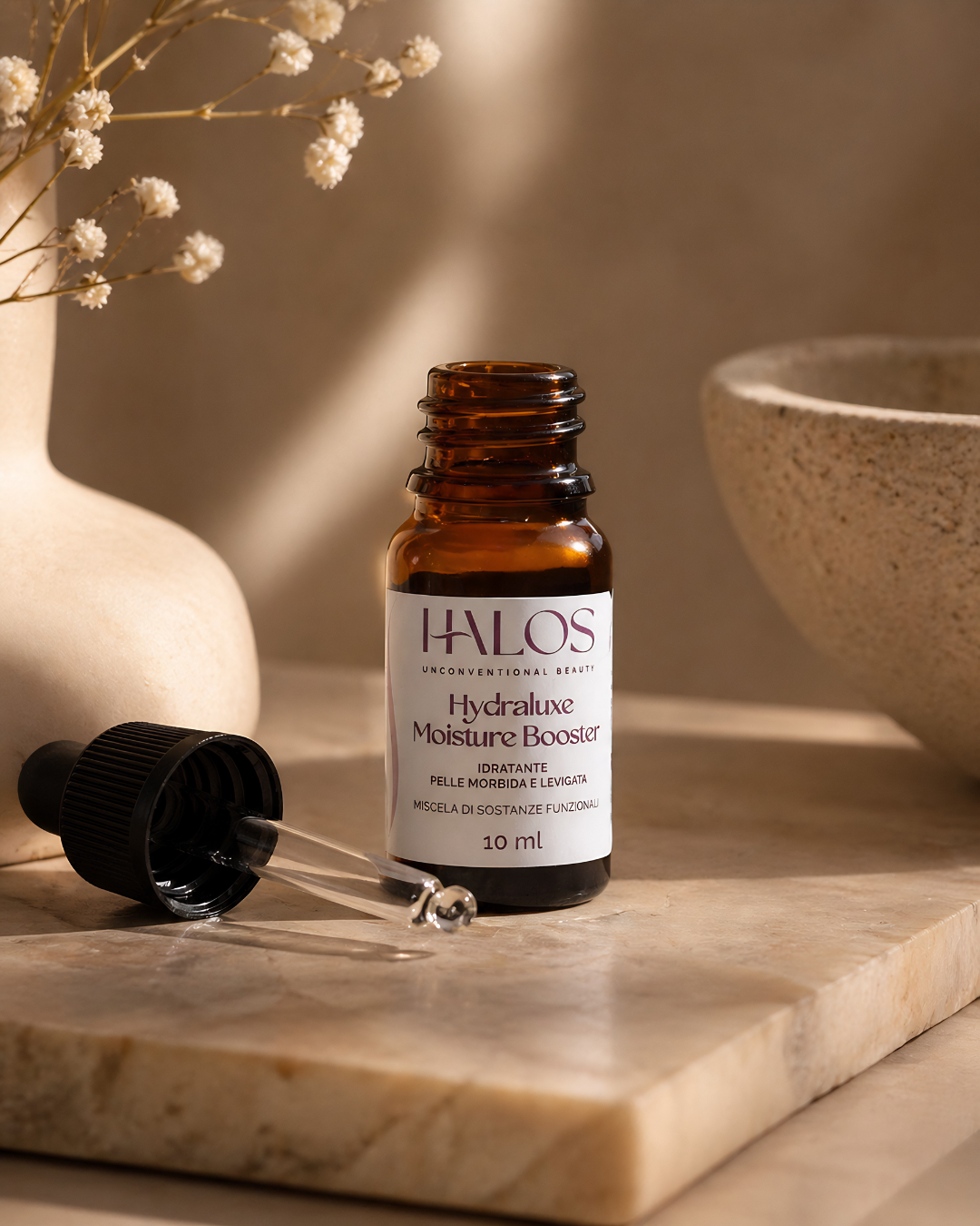 Flacone aperto e contagocce di Hydraluxe Moisture Booster su una base in pietra